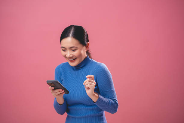 istock Asian woman enjoying using smartphone, isolated over pink background. 1808882167