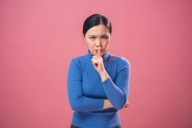 アジアの女性は眉をひそめ、ピンクの背景に隔離された唇に人差し指を置きます。 - hand sign stop gesture talking discussion ストックフォトと画像