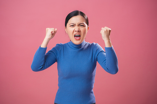 Asian woman feel angry annoyed shouting and looking at camera standing isolated on pink background.