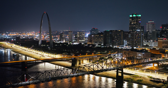 Aerial still image of The Gateway Arch behind Eads Bridge and Martin Luther King Bridge, taken by a drone on a hazy night in St. Louis, Missouri.
