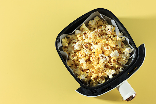 Top View Air Fryer Tray with Butter Popcorn on Yellow Table Background, Copy Space for Text