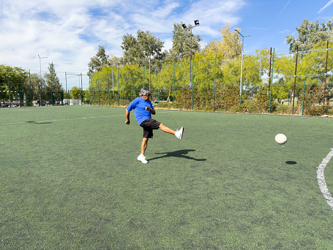 Elderly man is on the field kicking the soccer ball