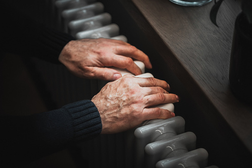 Cold at home. A man tries to warm his hands on a radiator