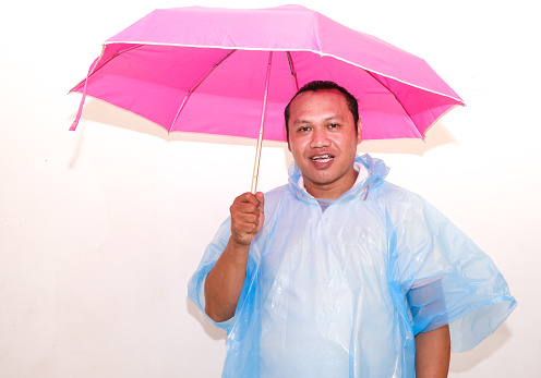 Asian man wearing blue raincoat and pink umbrella isolated on white background