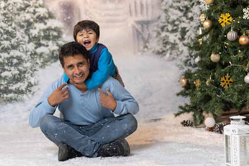 Mexican son hugging his father and laughing on christmas background