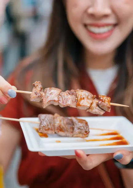 Crop shot asia smile women with Wagyu A5 Steak stick with BBq sauce and pepper Osaka japan streetfood