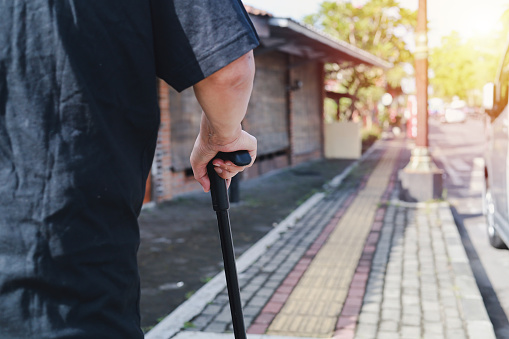 Close up photo of elderly man's hand using walking stick on the sidewalk in the morning