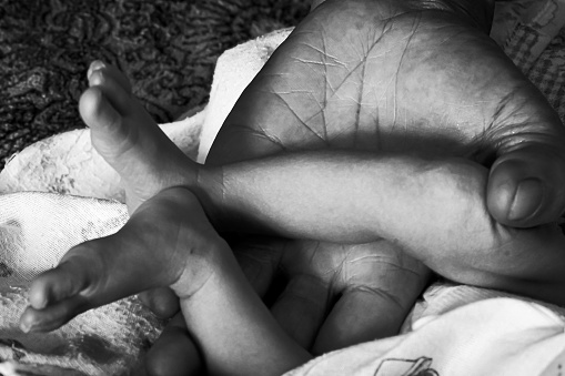 A close up image of a newborn baby's tiny fingers wrapped around dad's finger. Copy space in black background.