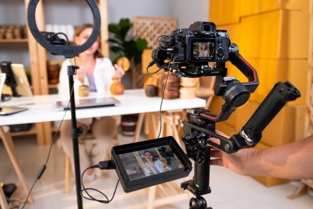 Behind the scenes of A young pretty woman entrepreneur live streaming to sale craft products to customers via filming professional camera stock photo