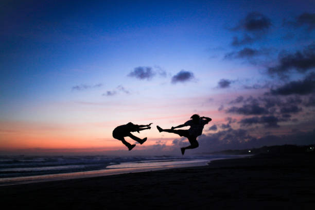 Silhouette of mother and children jumping at sunset on a beach. People jumping with hands raised on a sunset beach with the sea in the background. Amazing sunset in the Adriatic sea.