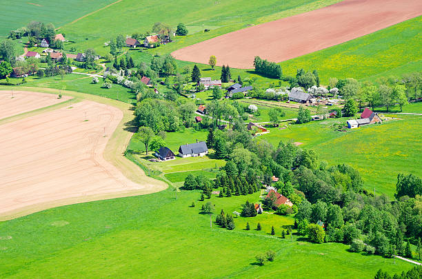 Aerial photograph over suburban family homes surrounded by picturesque patchwork quilt of crops field and green farm pasture.