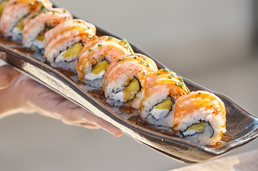 Closeup of anonymous person holding delicious Philadelphia maki rolls served with sauce on ceramic tray