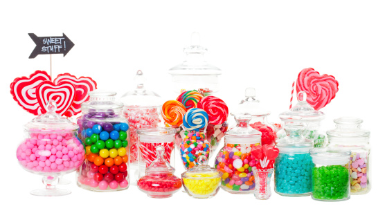 A candy buffet with a wide variety of candies in apothecary jars.  Shot on white background.