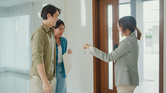 Young Asian woman real estate broker giving house keys to client after signing agreement contract. Buying a new house concept.