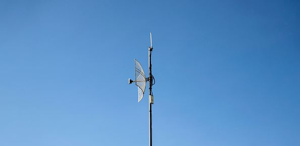 Internet wireless wifi receiver and repeater installed on metal pole on the roof of the building to service internet to users in local village, soft and selective focus.