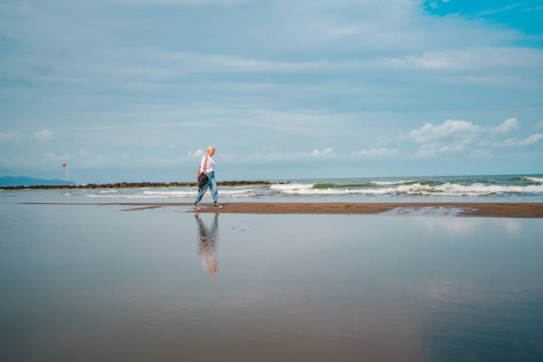 White haired woman walking next to sea at beach.