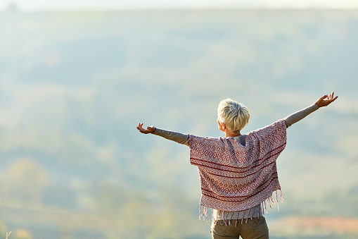 Rear view of a senior woman enjoying in autumn day with her arms outstretched. Copy space.