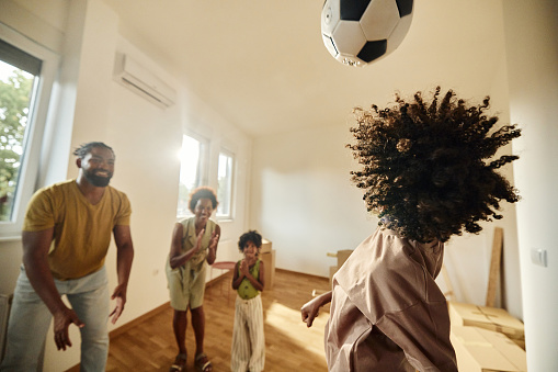 Happy African American father and son playing soccer while mother and daughter are cheering for them after moving into a new apartment.