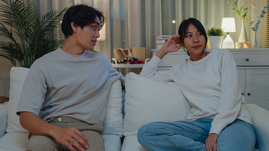 Young Asian couple arguing and fighting quarrel together sit on couch in living room at home night. Lifestyle spend time in house concept.
