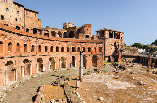 Circular courtyard of Trajan's Market, an ancient archeological site and Roman forum with brick buildings and columns, along the Victor Emmanuel modern monument and the Colosseum in Rome, Italy