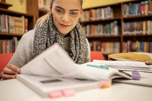 Young woman student reading a book and preparing for exams in college library