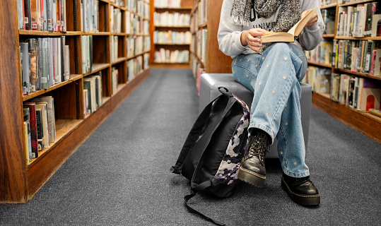 Low angle view of a female student sitting in library and reading a book at university after class