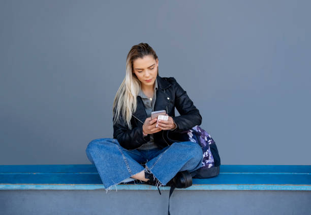 istock Pretty woman sitting by grey wall and using a phone 1809117271