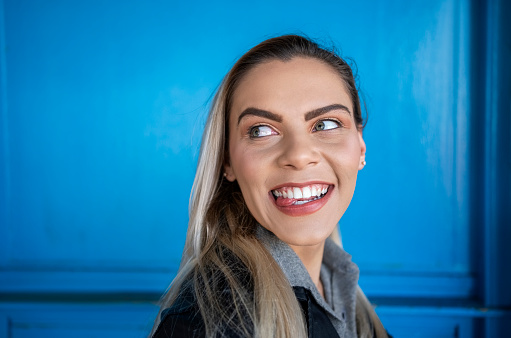 Portrait of beautiful young woman sticking out her tongue and looking over her shoulder while standing against blue wall