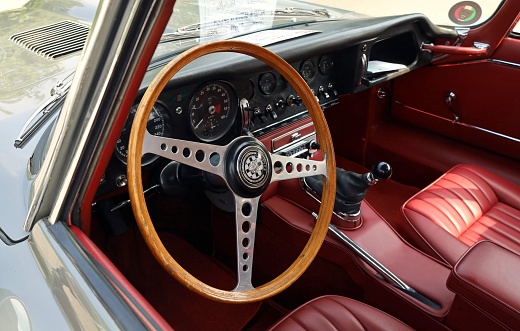 Udine, Italy. June 10, 2023. Wooden steering wheel and black dashboard of Jaguar E-Type , british sport car from Sixties, during a vintage car gathering.