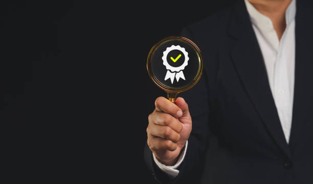istock Businessman holding a magnifying glass with the best quality symbol assurance icon while standing against a black background 1809149122