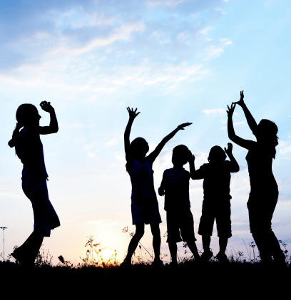 Silhouette group of happy children playing on meadow at sunset in summertime
