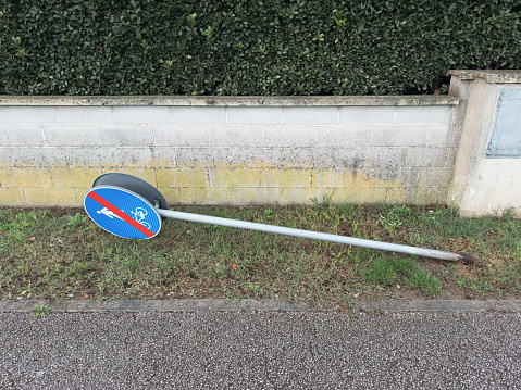 sign indicating the end of a pedestrian and cycle road in Italy. The sign is partially hidden by grass. Its metal pole, once upright, is now bent, grounding the sign.