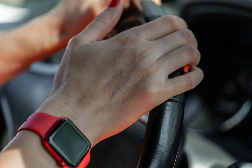 Women's hands with a smart watch hold the steering wheel of a car.
