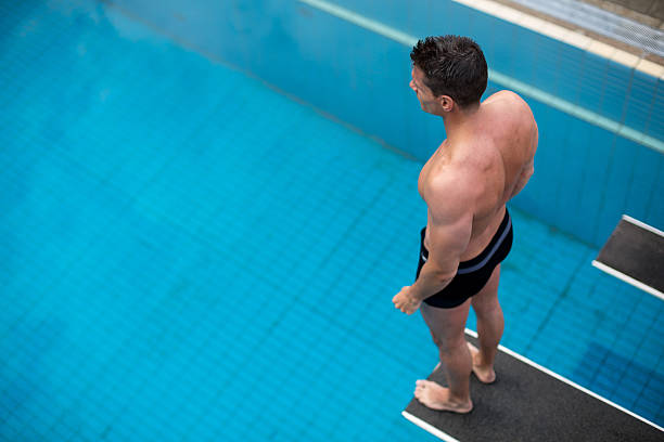 Man standing on diving board at public swimming pool above the water