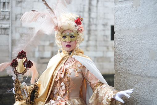 Venice, Italy - February 16 2023: Portrait of fully masked person standing by stone wall of an old building in Venice and rehearsing, time of traditional winter Carnival, Veneto, Europe