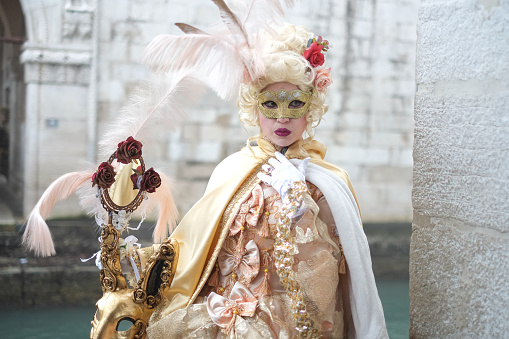 Venice, Italy - February 21, 2022: The Carnival of Venice, when visitors and residents of Venice dress up in wonderfully elaborate costumes and parade through the squares and along the banks of the canals. Here we see once such celebrant in a spectacular gold and green outfit.