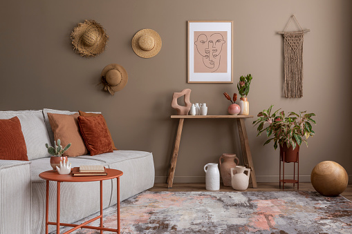 Creative composition of living room interior with mock up poster frame, wooden consola, round coffee table, beige sofa, plants, terracota pillow and personal accessories. Home decor. Template.