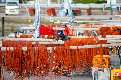 Nachikatsuura, Japan; 1st October 2023: Fishermen mending their fishing nets at Katsuura Harbor in Wakayama.