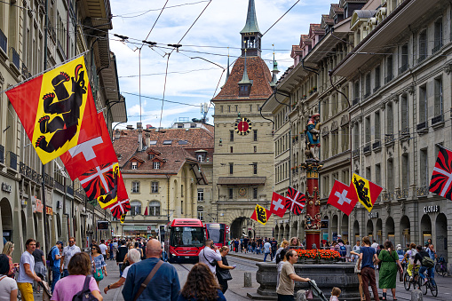 Hospital Alley at the old town of Swiss City of Bern with tramway, pedestrians and clock tower in the background on a cloudy summer day. Photo taken July 1st, 2023, Bern, Switzerland.
