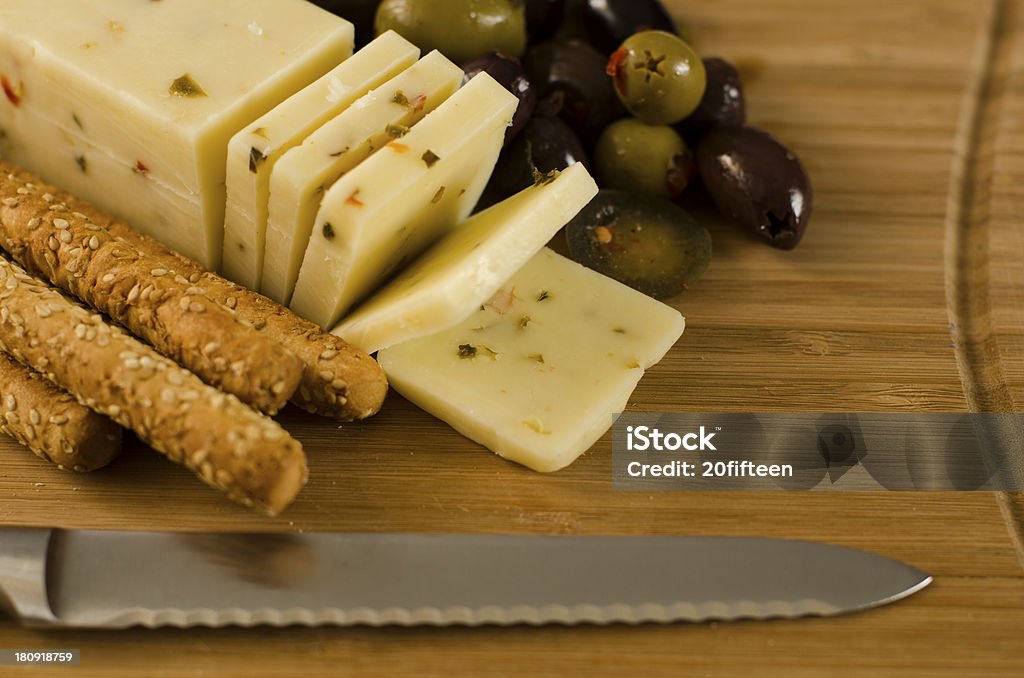 Pepper Jack, Sesame Seed Breadsticks, Mediterranean Olives, Hot Peppers Sliced Pepper Jack cheese with sesame seed breadsticks, Mediterranean olives and hot peppers on a wooden cheese board with serated knife out of focus in the foreground Monterey Jack Cheese Stock Photo