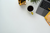 Top view a cup of coffee, laptop computer, books and pencil holder on white table.