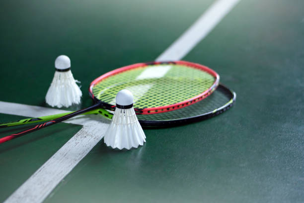 Badminton play badminton rackets and white feather shuttlecocks on green cement floor of indoor badminton court, soft focus, popular indoor sports concept. badminton racket stock pictures, royalty-free photos & images