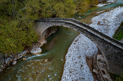 Drone aerial of Ancient, stoned, arched bridge St. Vissarion on the Portaikos river in autumn. Trikalla pyli village Thessaly Greece