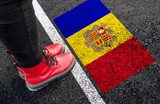 a womman with a boots standing on asphalt next to flag of Andorra and border