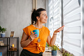 Young Woman Drinking Coffee While Looking Out The Window At Home