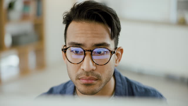 Glasses, reading and young businessman in the office doing creative research for startup company. Professional, technology and male designer working on a project with laptop in modern workplace
