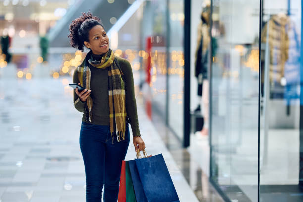 istock Happy black woman using cell phone while window shopping at the mall. 1809292734