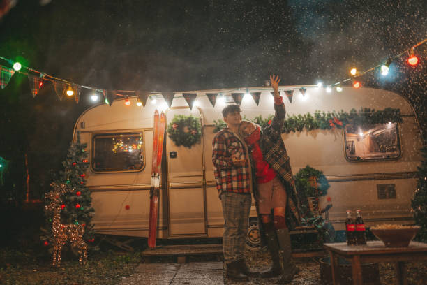 Happy couple in love together rejoices at first snow hugging near Xmas camper trailer Happy couple celebrating Christmas and New Year winter holidays season in Camper Park. Young joyful couple spending time together hugs and kisses rejoices at first snow near Xmas camper trailer Christmas  Let It Snow stock pictures, royalty-free photos & images