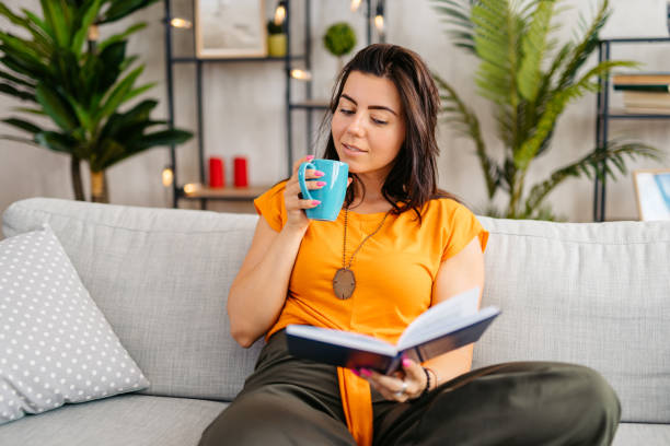 istock Young Woman Drinking Coffee And Reading A Book At Home 1809296506