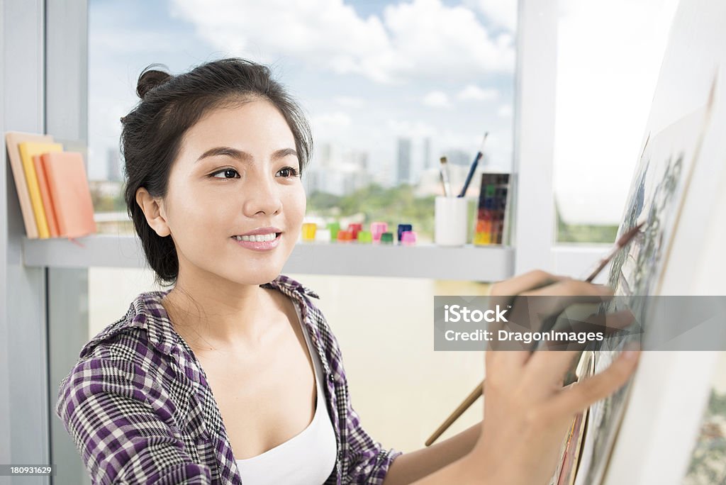 Young woman enjoying painting as a hobby Close-up image of a lovely artist busy with painting on the foreground Adult Stock Photo